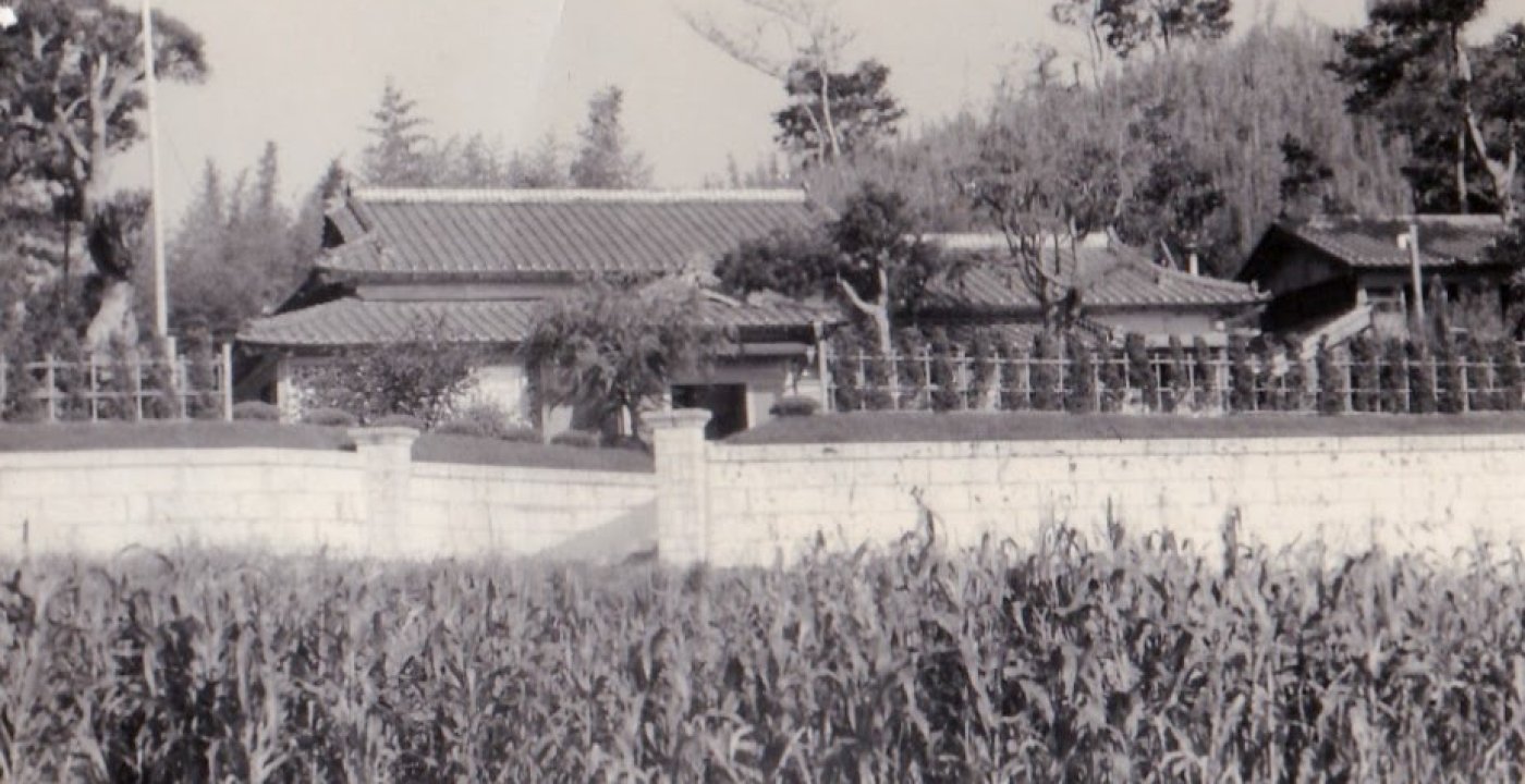 Historic black and white photograph of the farmhouse behind a field